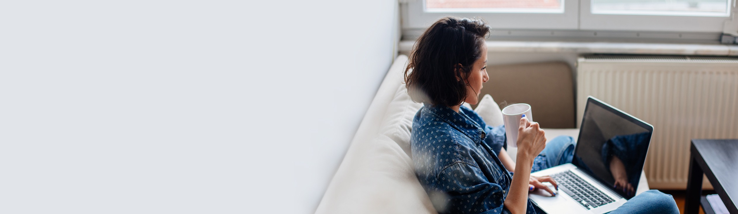 A woman sitting on a couch with a laptop, holding a mug.