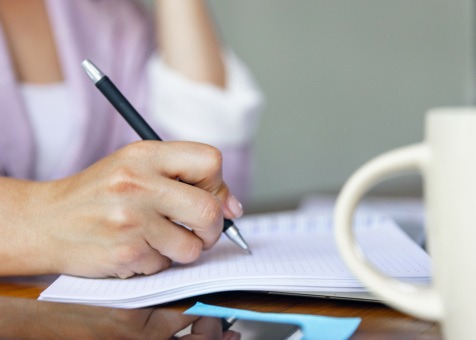 A close-up image of a women writing on a notebook.